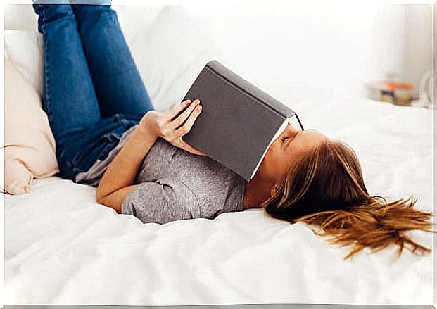 Girl in bed smelling a book.