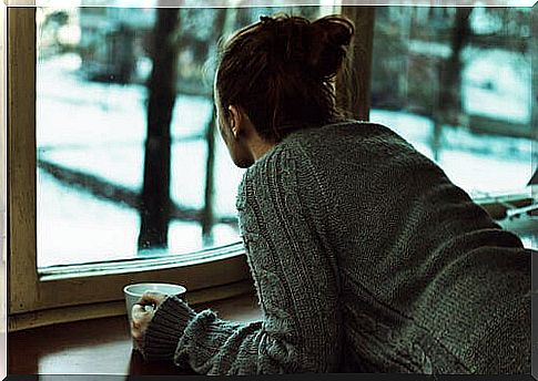Woman drinking coffee at a window thinking about loneliness